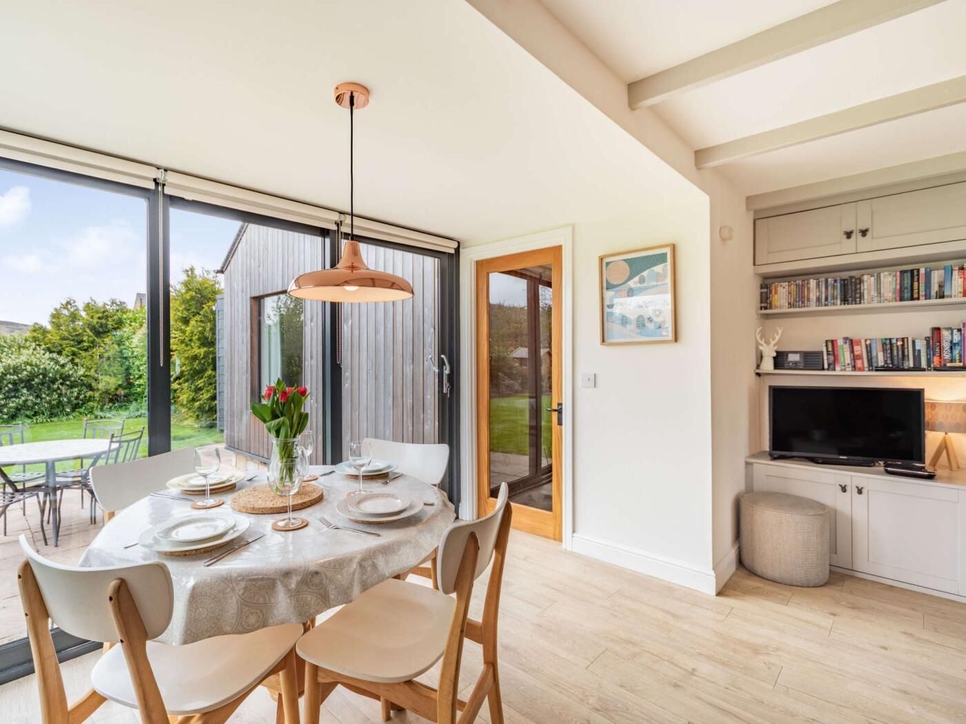 A dining area with a table set for four, a pendant light, and a view of the garden through a sliding door.