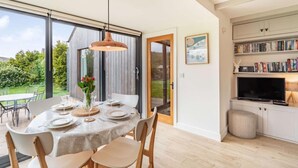 Un coin repas avec une table dressée pour quatre personnes, un luminaire suspendu et une vue sur le jardin grâce à une porte coulissante.