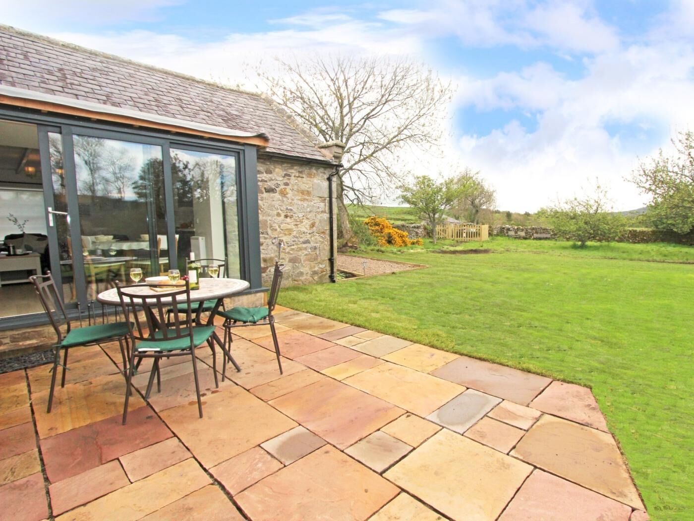 A patio with a table and chairs, a stone wall, and a grassy yard.