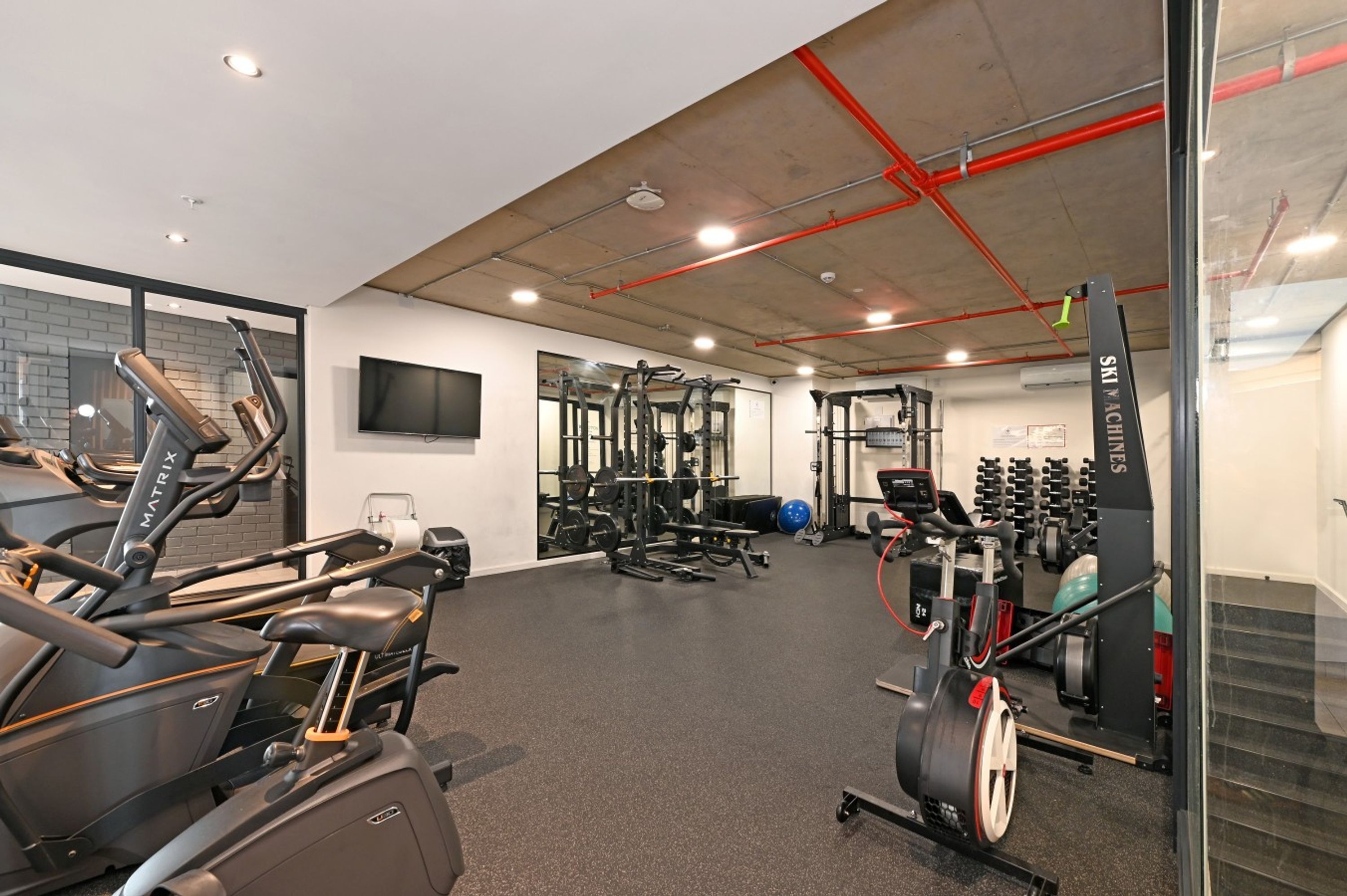 A gym with cardio machines, weightlifting equipment, and a television on the wall.