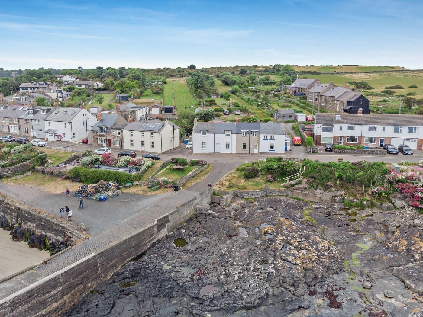 A coastal town with residential buildings, a rocky foreground, and a clear sky.