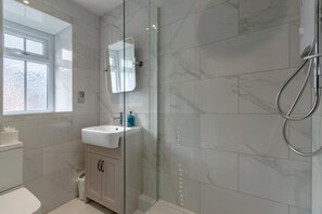 Een moderne badkamer met een douchecabine van glas, een witte wastafel en een spiegel erboven.