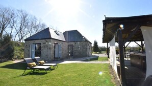 Un bâtiment en pierre doté d’un toit en pente, d’un patio couvert et d’une pelouse aménagée avec des chaises longues.