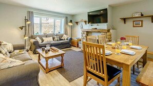 A cozy living room with a sofa, a dining table set for two, and a TV mounted above the fireplace. - 3 Bed in Beadnell (oc-cn119) (Beadnell)