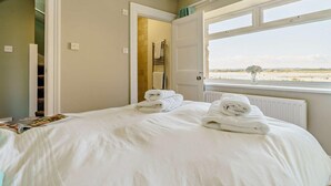 A hotel room with a bed, a window with a view of the beach, and a door leading to a bathroom. - 3 Bed in Beadnell (oc-cn119) (Beadnell)