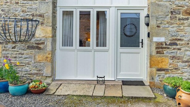 A stone building with a white double door, a wreath on the door, and potted plants outside. - 4 Bed in Consett (oc-cn108) (Hunstanworth)