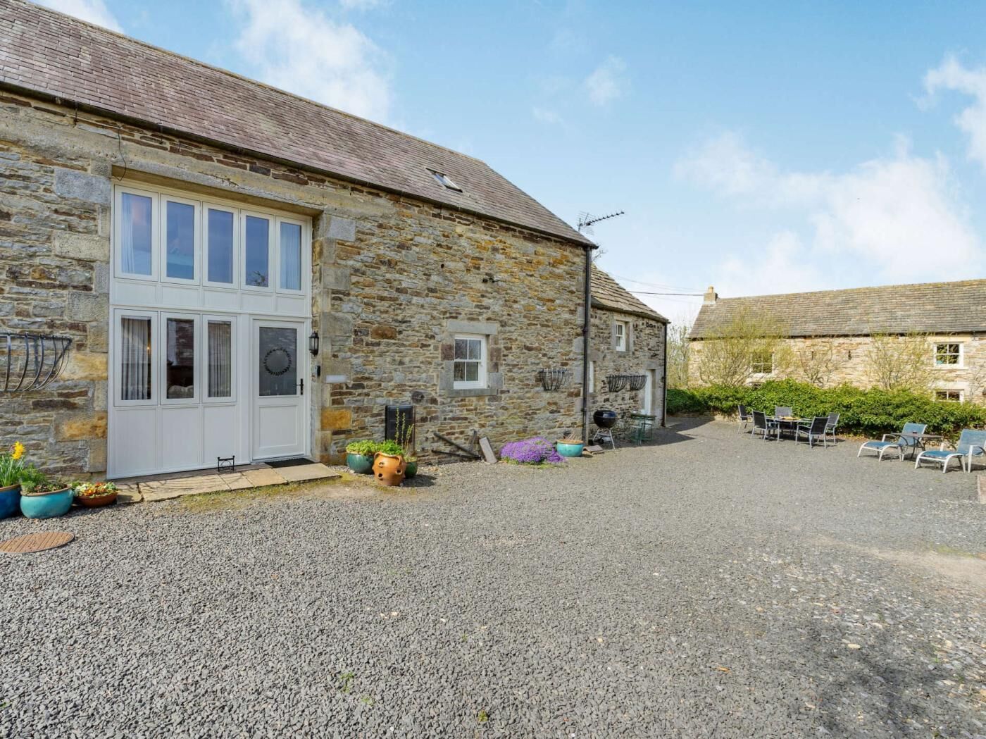 A stone building with a white door, a gravel driveway, and outdoor seating.