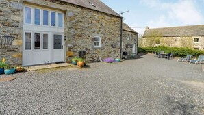 A stone building with a white door, a gravel driveway, and outdoor seating. - 4 Bed in Consett (oc-cn108) (Hunstanworth)