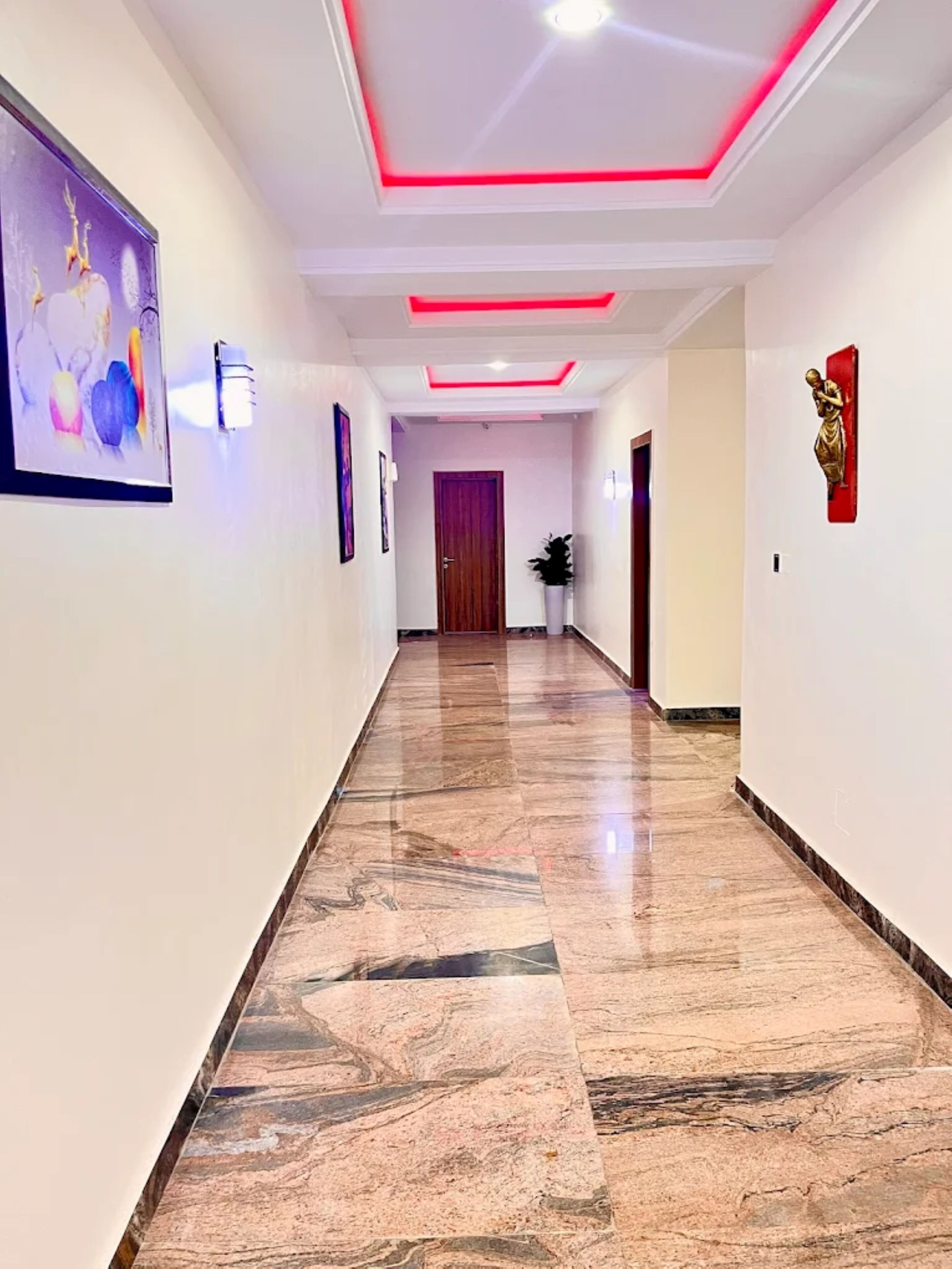 A hallway with a marble floor, a wooden door at the end, and a red accent wall.