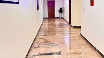 A hallway with a marble floor, a wooden door at the end, and a red accent wall.