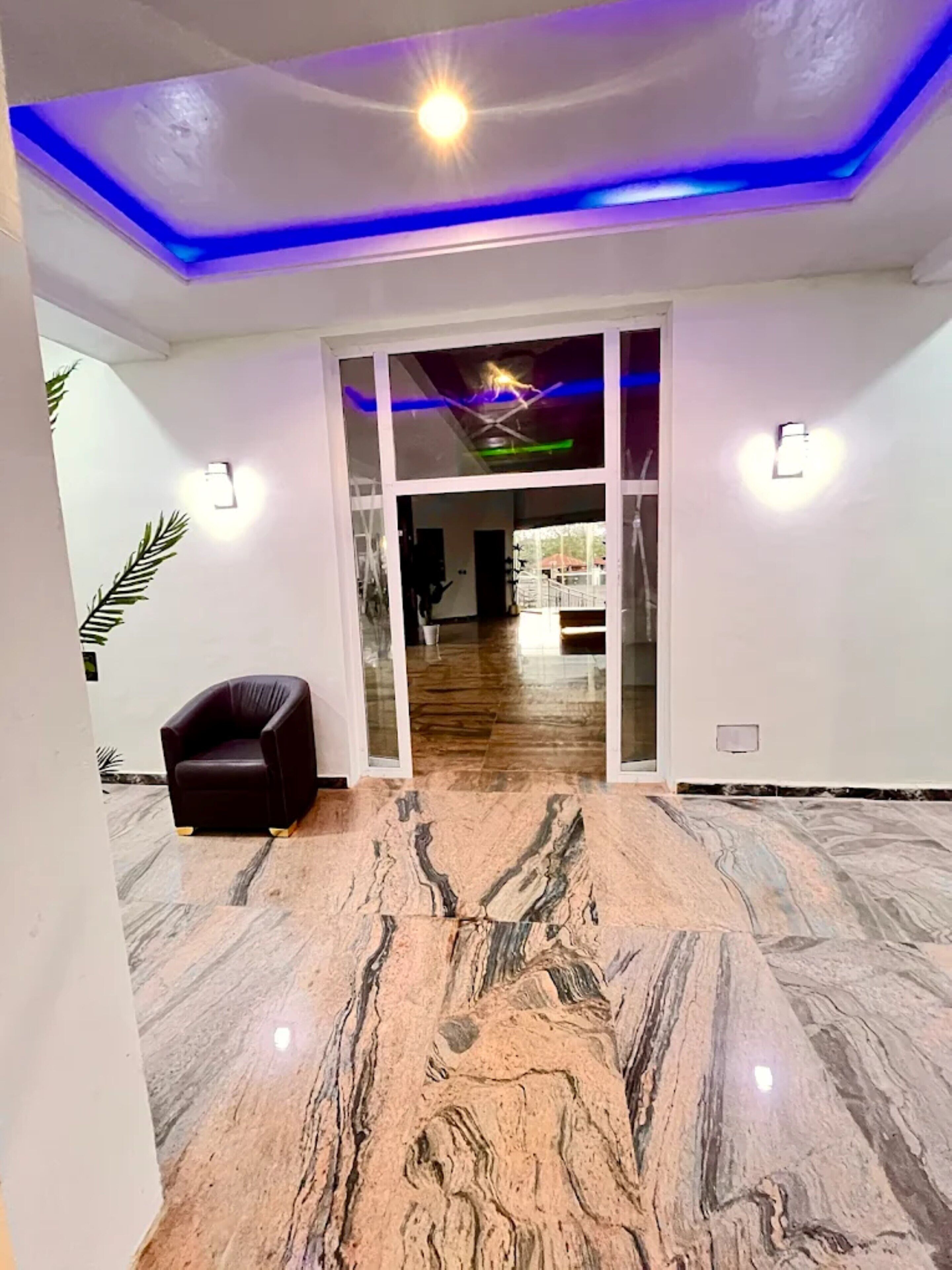Un interior moderno con suelo de mármol, un sillón de cuero e iluminación LED azul en el techo.