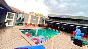 A pool area with a wooden deck, lounge chairs, and a bar area.