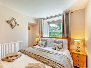 Une chambre à coucher comprenant un lit, deux tables de chevet, une fenêtre avec des rideaux, un radiateur et un cadre photo fixé au mur.