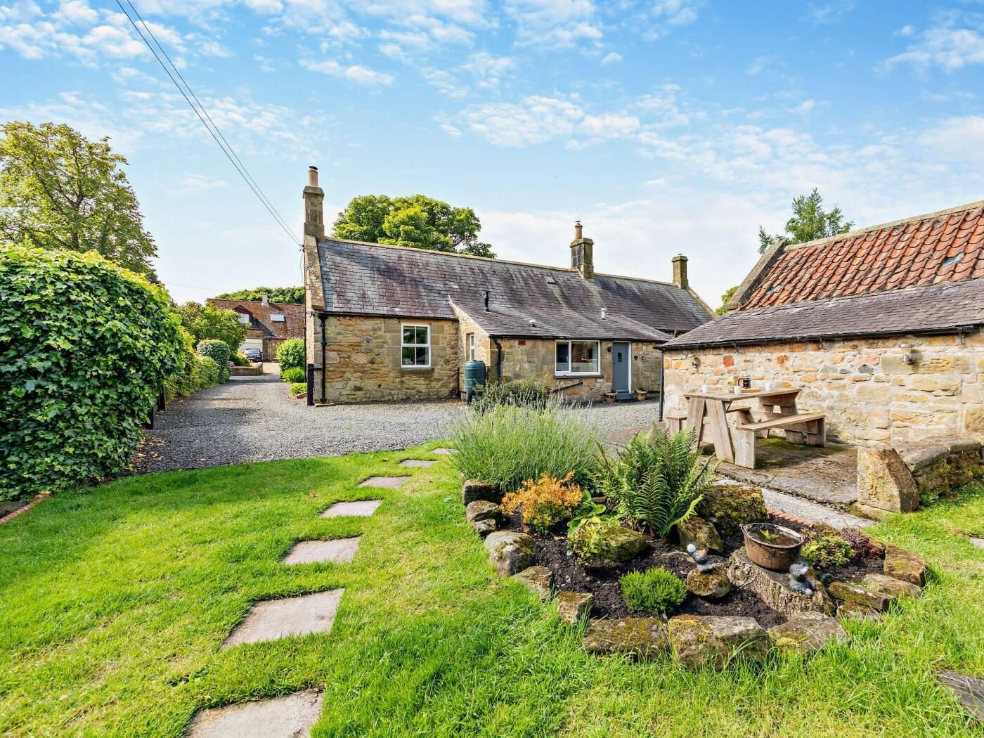 A stone cottage with a gravel driveway, a garden with stepping stones, and a small outdoor seating area.