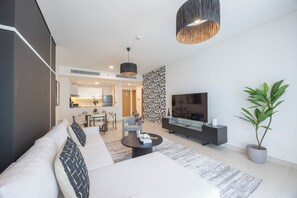 A modern living room with a sofa, TV, and a dining area in the background. - Bloomfields 1BR in Radiant Viewz 1  (Abu Dhabi)