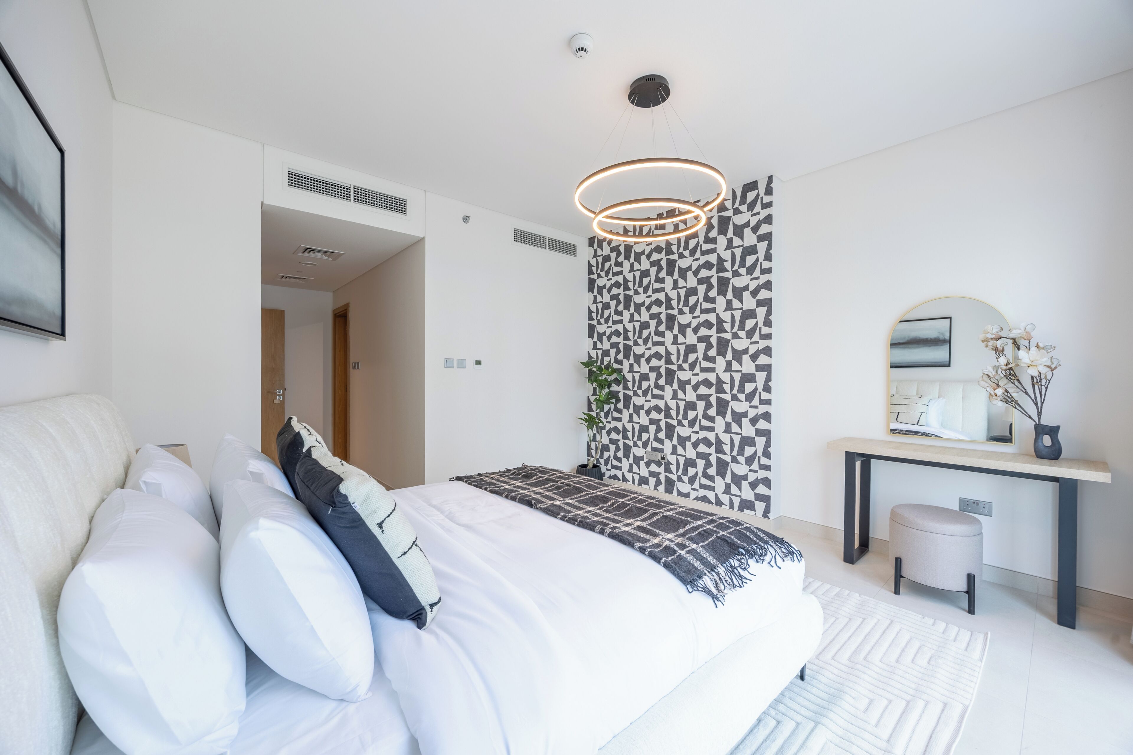 Une chambre moderne avec un grand lit, un bureau et un mur décoré d’un motif.