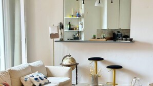 A modern living room with a sofa, a round coffee table, a bar stool, and a kitchen area with a mirror above the counter. - Celine 8 (Paris)