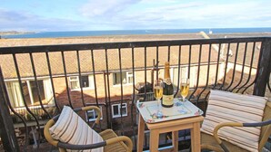 A balcony with wicker furniture, a table with a bottle of champagne and glasses, and a view of the sea. - 3 Bed in Seahouses (oc-cn112) (Seahouses)