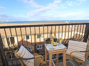 Ein Balkon mit Korbmöbeln, ein Tisch mit einer Champagnerflasche und Gläsern sowie Meerblick.