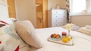 A hotel room with a bed, a bedside table with a tray of croissants, orange juice, and a flower arrangement. - 3 Bed in Seahouses (oc-cn112) (Seahouses)