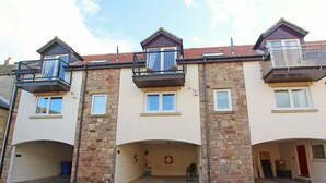 A multi-story residential building with stone facades, balconies, and a covered entrance. - 3 Bed in Seahouses (oc-cn112) (Seahouses)