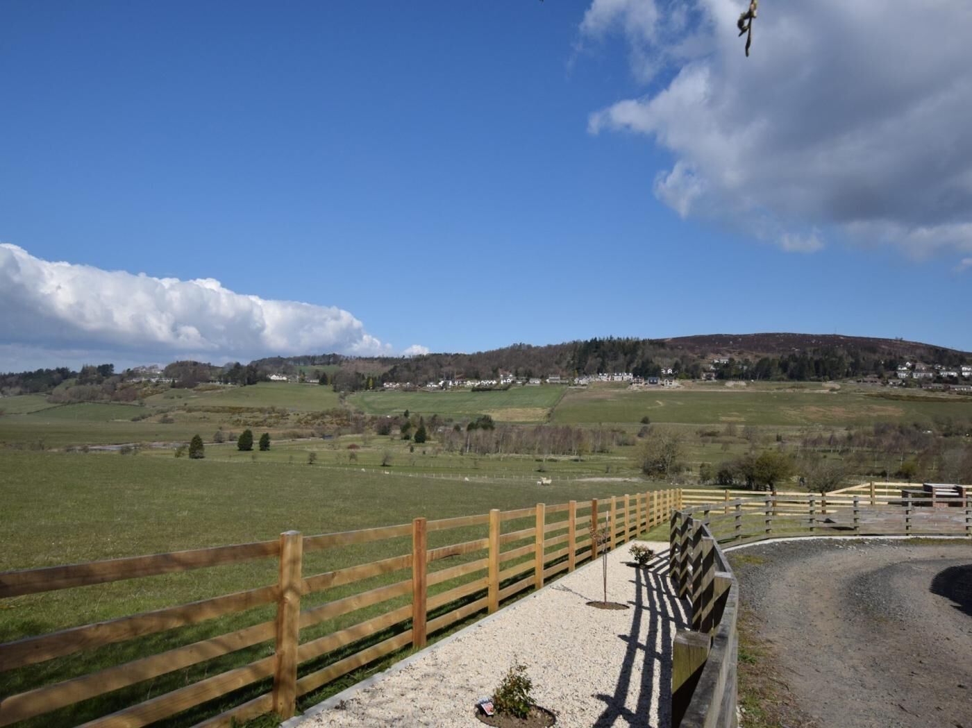 Un paysage rural avec une clôture en bois, un chemin de gravier et une colline en arrière-plan.