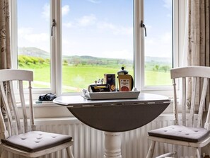 Ein Zimmer mit Tisch und zwei Stühlen, ein Fenster mit Blick auf grüne Felder und einer Heizung.