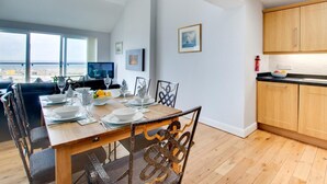 A modern dining area with a wooden table set for four, a television in the background, and a kitchen with wooden cabinets. - 3 Bed in Seahouses (oc-cn120) (Seahouses)