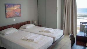 Habitación de hotel con dos camas, un armario grande, un escritorio y vista al mar.