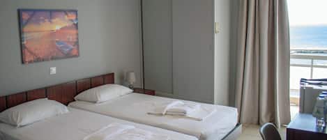 Habitación de hotel con dos camas, un armario grande, un escritorio y vista al mar.