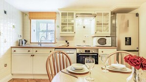 Une cuisine avec des meubles blancs, un four à micro-ondes, un four traditionnel et une table à manger pour deux personnes.