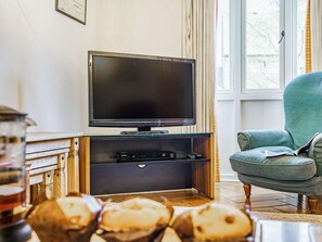 A living room with a flat-screen TV, wooden entertainment unit, a green armchair, and a window with curtains. - 3 Bed in Consett (oc-cn110) (Hunstanworth)