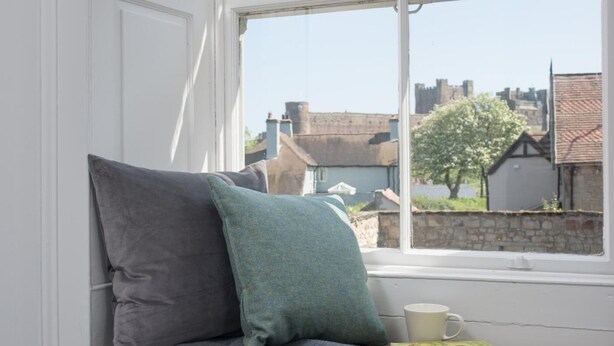 Asiento junto a la ventana con cojines, un libro y una taza.