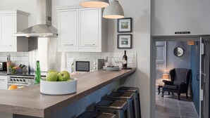 Una cocina moderna con una isla central, taburetes de bar, microondas y una botella de vino.