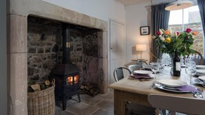 Una chimenea de piedra con estufa de leña moderna, una mesa de comedor con platos y vasos, y un florero con flores.