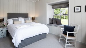 Un dormitorio con cama, mesitas de noche, una silla, ventana con vistas y una lámpara colgante.