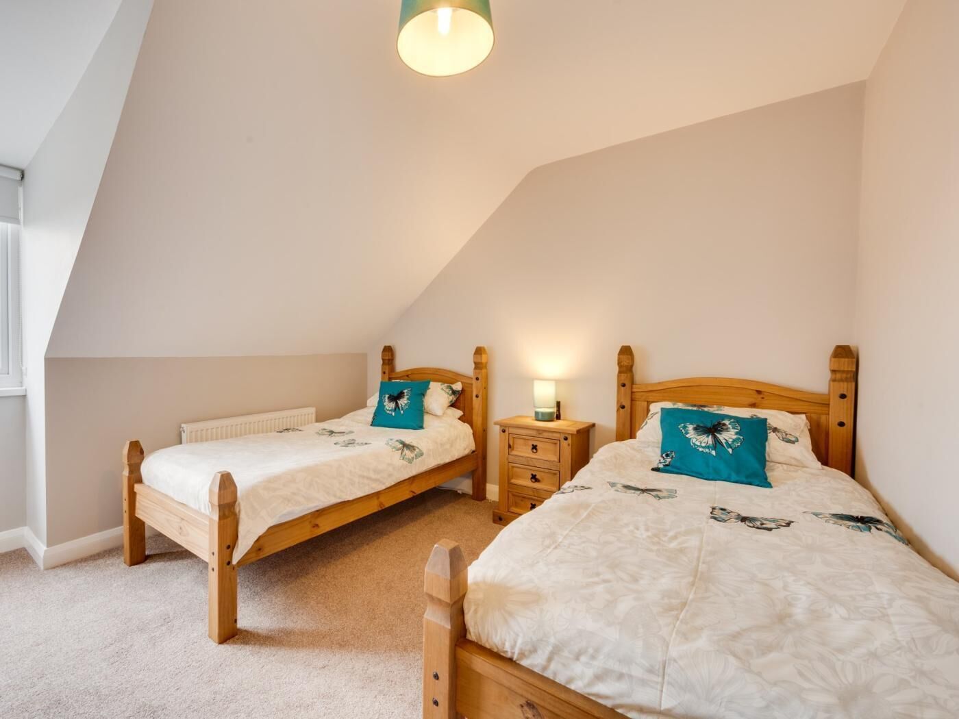 A bedroom with two wooden beds, a nightstand with a lamp, and a radiator.