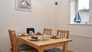 A dining table with chairs, plates of food, and a framed picture on the wall. - 2 Bed in Seahouses (oc-cn135) (Seahouses)