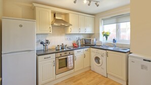 A kitchen with white cabinets, a refrigerator, an oven, a microwave, a washing machine, and a window with a view. - 2 Bed in Seahouses (oc-cn135) (Seahouses)