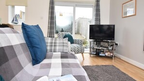 A living room with a sofa, a television, and a bookshelf. - 2 Bed in Seahouses (oc-cn135) (Seahouses)