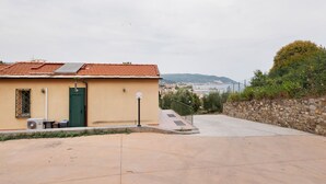 A building with a tiled roof, a green door, and a small outdoor area with a paved path leading to a stone wall.
