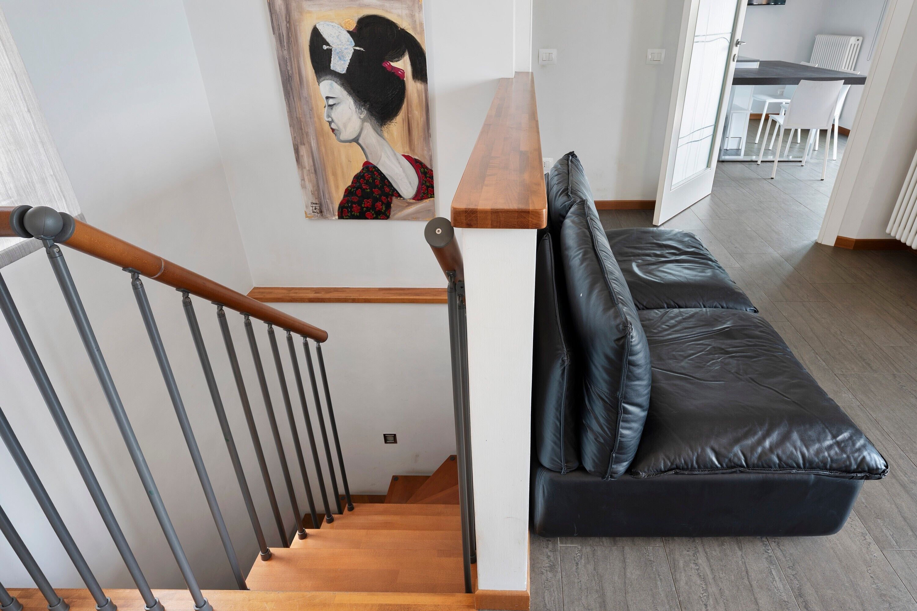 Un escalier avec des marches en bois et des rampes en métal, un canapé en cuir noir avec des coussins et un tableau accroché au mur.
