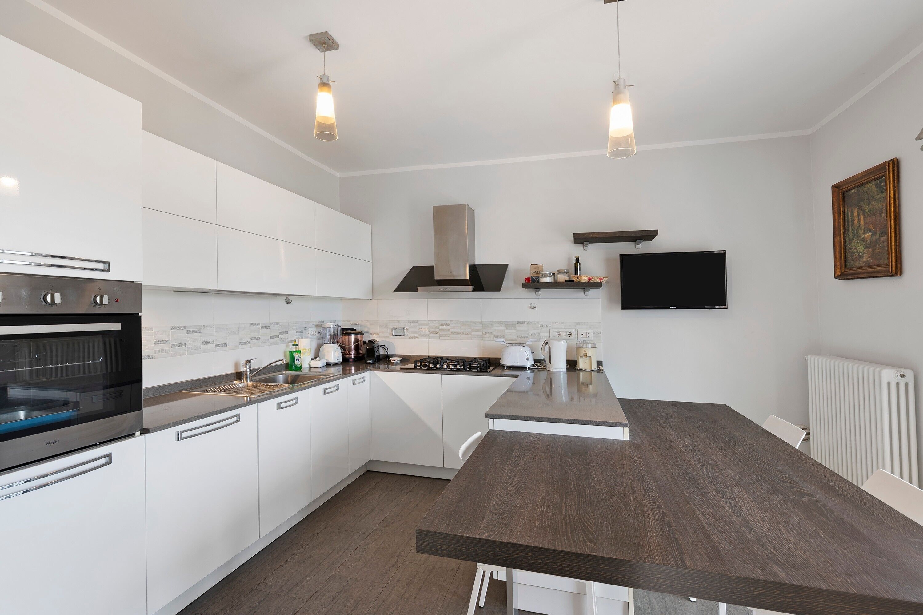Una cocina moderna con armarios blancos, horno empotrado, estufa y una isla grande con encimera oscura.