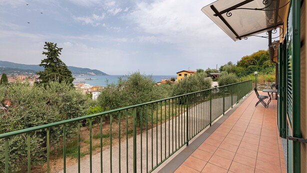 A balcony with a view of the sea, a green railing, and outdoor furniture.