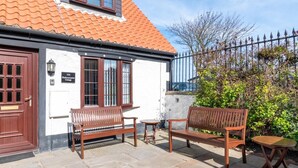 Ein Cottage mit einem Ziegeldach, einer Holztür und einer Sitzgelegenheit mit einem kleinen Tisch.