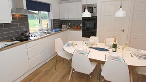 A modern kitchen with white cabinets, a dining table set for four, and a view of the outdoors. - 3 Bed in Alnwick (oc-cn132) (Christon Bank)