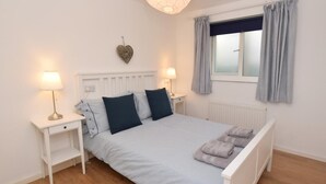 A neatly arranged bedroom with a bed, bedside lamps, a window with curtains, and a wall-mounted heart decoration. - 3 Bed in Alnwick (oc-cn132) (Christon Bank)