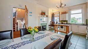 A dining area with a table set for four, a vase with flowers, and a staircase leading to another room. - 5 Bed in Tynemouth (oc-cn125) (Tynemouth)
