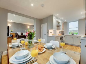 A modern dining area with a wooden table set for breakfast, including plates, glasses, and croissants. - 3 Bed in Beadnell (oc-cn113) (Beadnell)