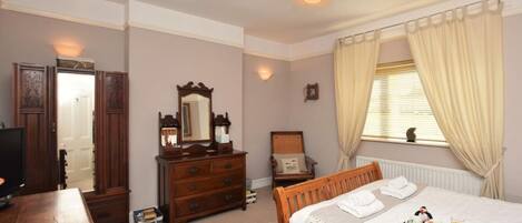 Quarto com cama de madeira, penteadeira, espelho, televisão e janela com cortinas.